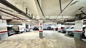 Useita kerroksia sisältävä pysäköintihalli, jossa on useita parkissa olevia autoja, betonilattiat ja näkyvät tukipalkit.