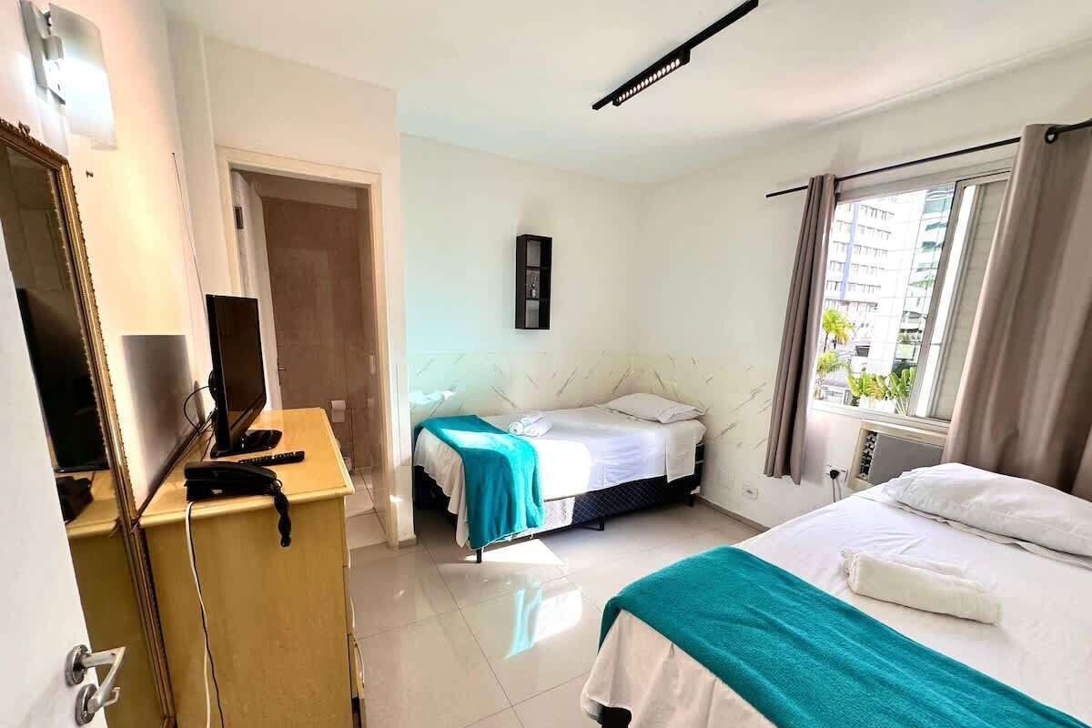 Ein Hotelzimmer mit einem Bett, einem Schreibtisch mit Computer und einem fensterbepflanzten Fenster.