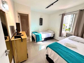 A hotel room with a bed, a desk with a computer, and a window with curtains. - Santa Mônica Residen (São Paulo)