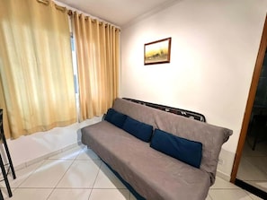 A room with a sofa, curtains, a framed picture, and tiled flooring. - Santa Mônica Residen (São Paulo)
