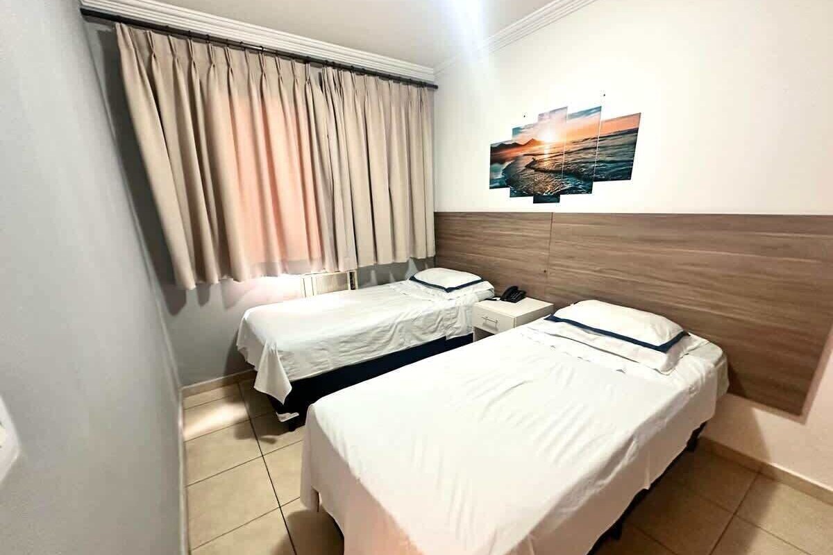 Ein Hotelzimmer mit zwei Einzelbetten, einem Holzkopfende, einem Nachttisch, einem Telefon und einem an der Wand befestigten Kunstwerk.