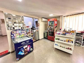 A pharmacy with shelves stocked with various products, a refrigerated display case, and a promotional stand for a sports brand. - Santa Mônica Residen (São Paulo)