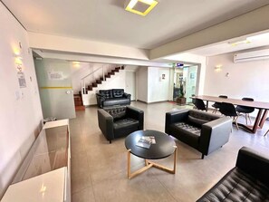 Amplia sala de estar con escalera, sofás de cuero negro, una mesa redonda de centro y una mesa de comedor con sillas.