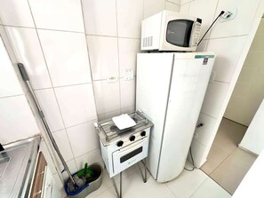 A compact kitchen with a gas stove, a microwave, and a refrigerator. - Santa Mônica Residen (São Paulo)