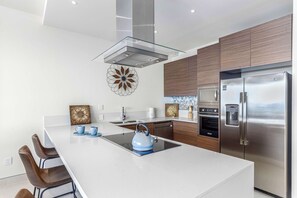 A modern kitchen with a central island, stainless steel appliances, and a decorative wall piece. - Two Condos | Ideal for Families & Groups (Cabo San Lucas)