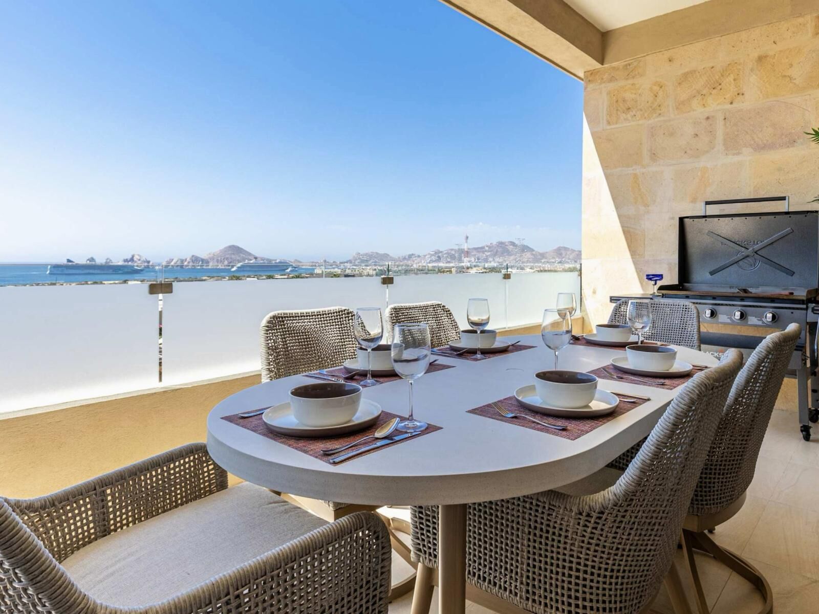 A round dining table with chairs, a grill, and a view of the sea.