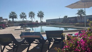 A poolside area with lounge chairs and an umbrella, surrounded by palm trees and flowers. - Two Condos | Ideal for Families & Groups (Cabo San Lucas)