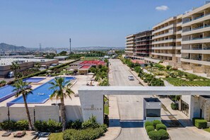 A hotel with a swimming pool, a parking area, and a view of the cityscape. - Two Condos | Ideal for Families & Groups (Cabo San Lucas)