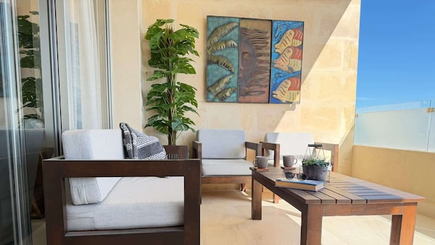 A balcony with two wooden chairs, a small table, a potted plant, and a painting on the wall. - Two Condos | Ideal for Families & Groups (Cabo San Lucas)
