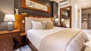 A hotel room with a large bed, bedside tables, a mirror, and a wardrobe. - Two Condos | Ideal for Families & Groups (Cabo San Lucas)