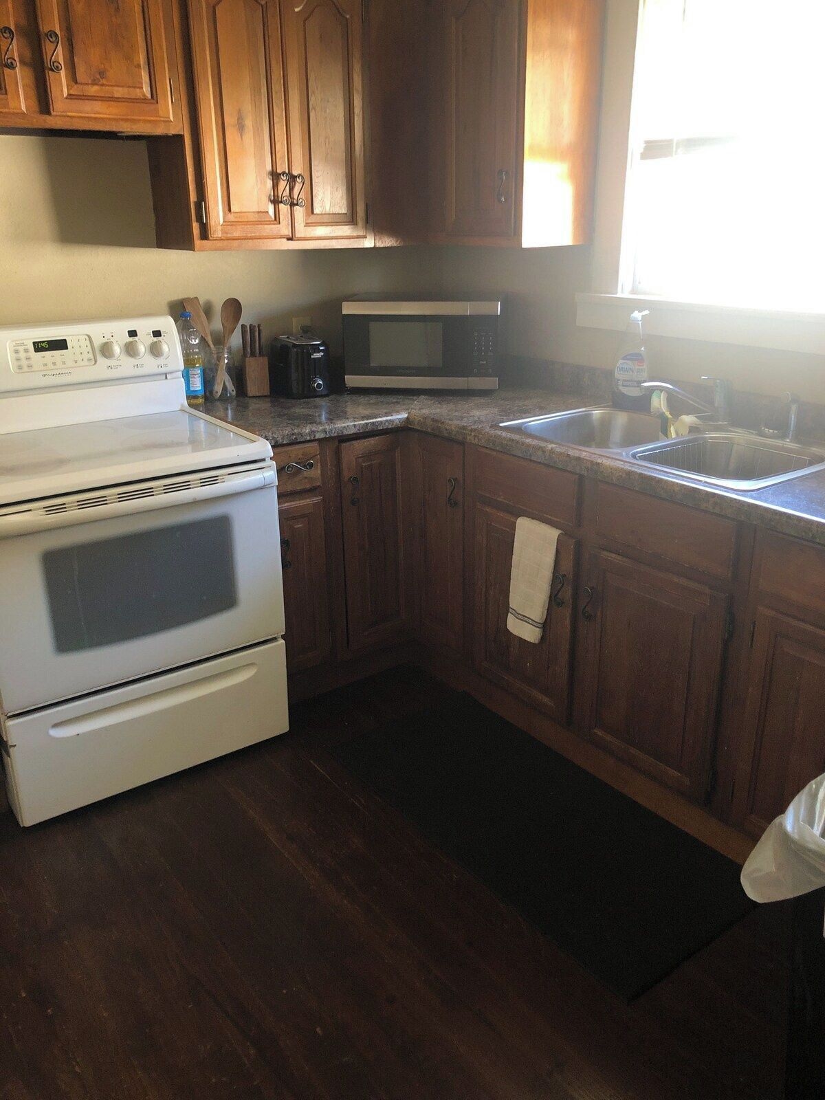A kitchen with wooden cabinets, a white stove, a microwave, and a sink.