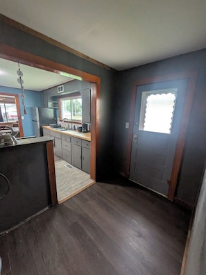 A compact kitchen with dark wood flooring, a central island, and a window with a white blind.