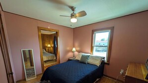 A bedroom with a bed, a ceiling fan, a window, and a mirror.