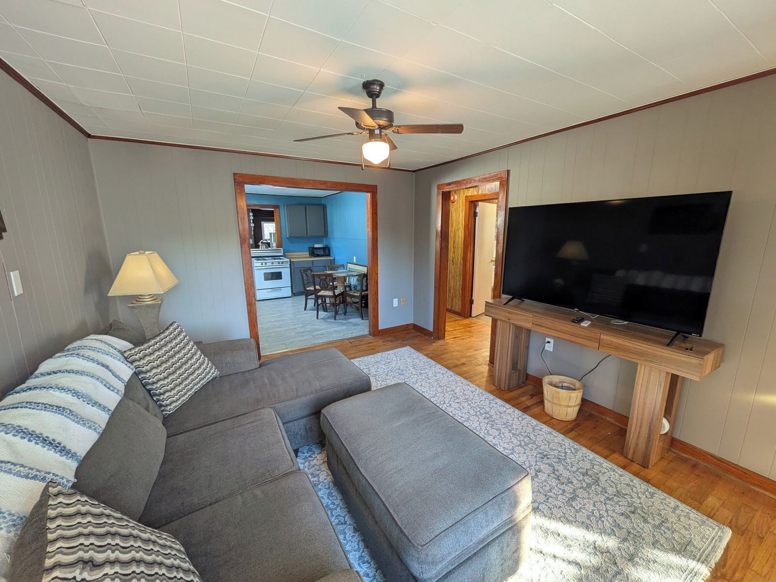 A living room with a sofa, ottoman, TV, and a ceiling fan.