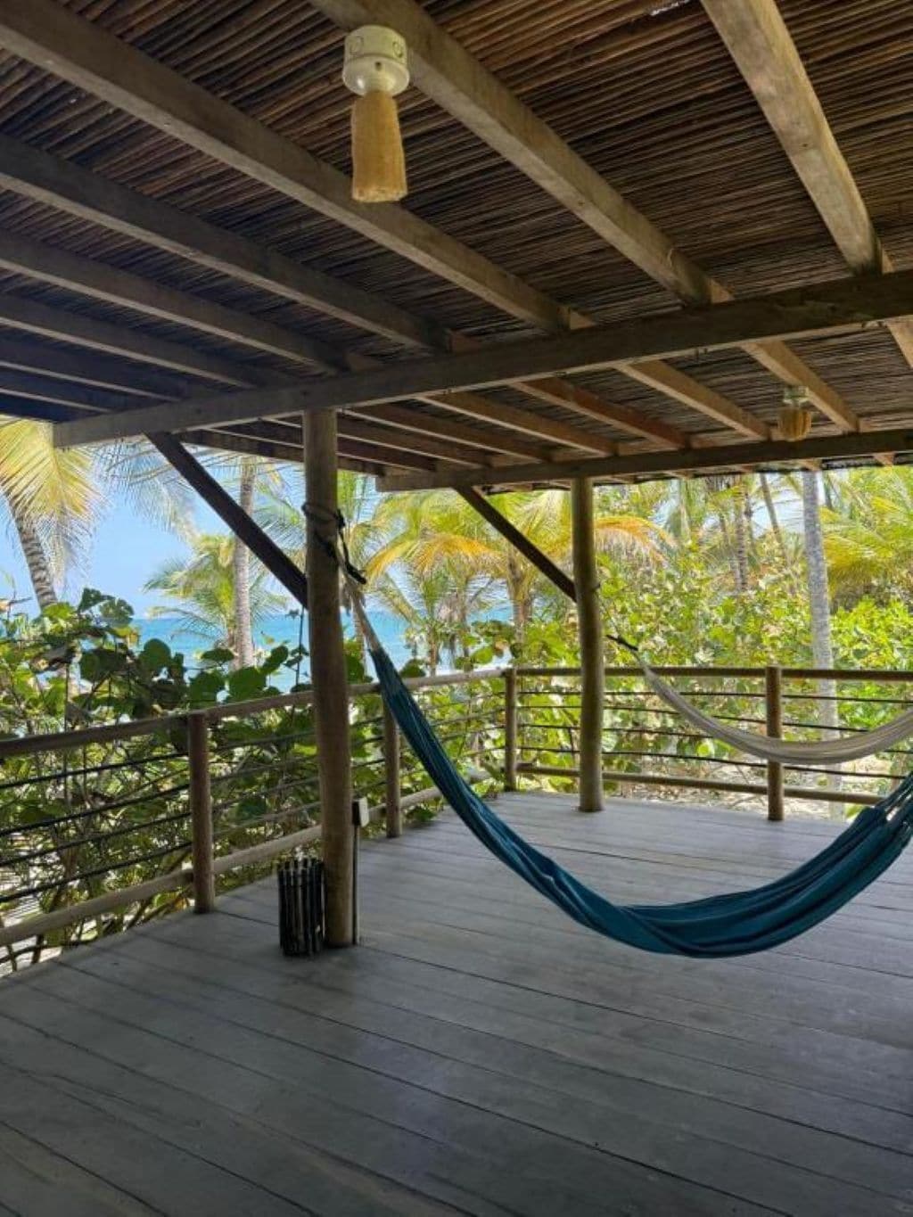 A wooden deck with a hammock, surrounded by palm trees and a clear view of the ocean.