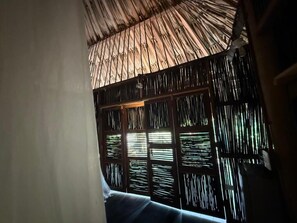 Una habitación con techo de paja, una ventana con persianas verticales y un sofá azul.