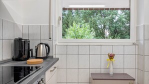 Una cocina con ventana, estufa, hervidor y un mueble pequeño.