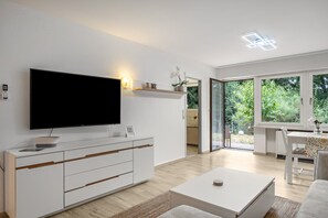 Ett modernt vardagsrum med en platt-TV, en vit soffa, ett soffbord och en matplats med ett bord och stolar.