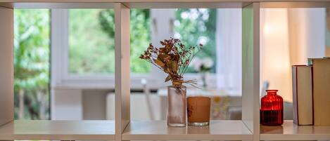 Ein Bücherregal mit einer Vase getrockneter Blumen, einer Kerze und einer roten Flasche.