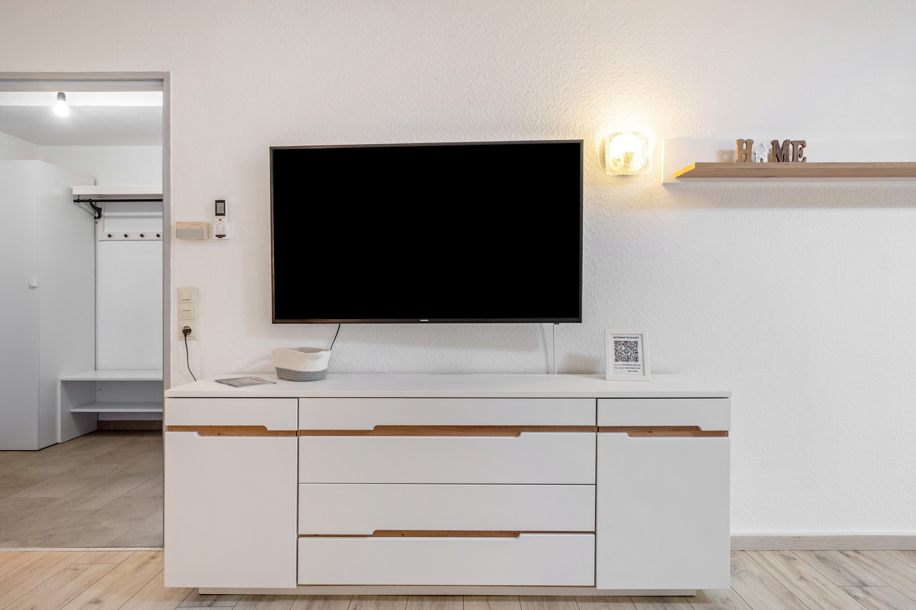 A modern, white entertainment unit with a flat-screen TV, a built-in sound system, and a shelf with decorative items.
