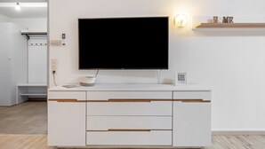 Un mueble moderno y blanco para entretenimiento con televisor de pantalla plana, sistema de sonido integrado y una repisa con objetos decorativos.