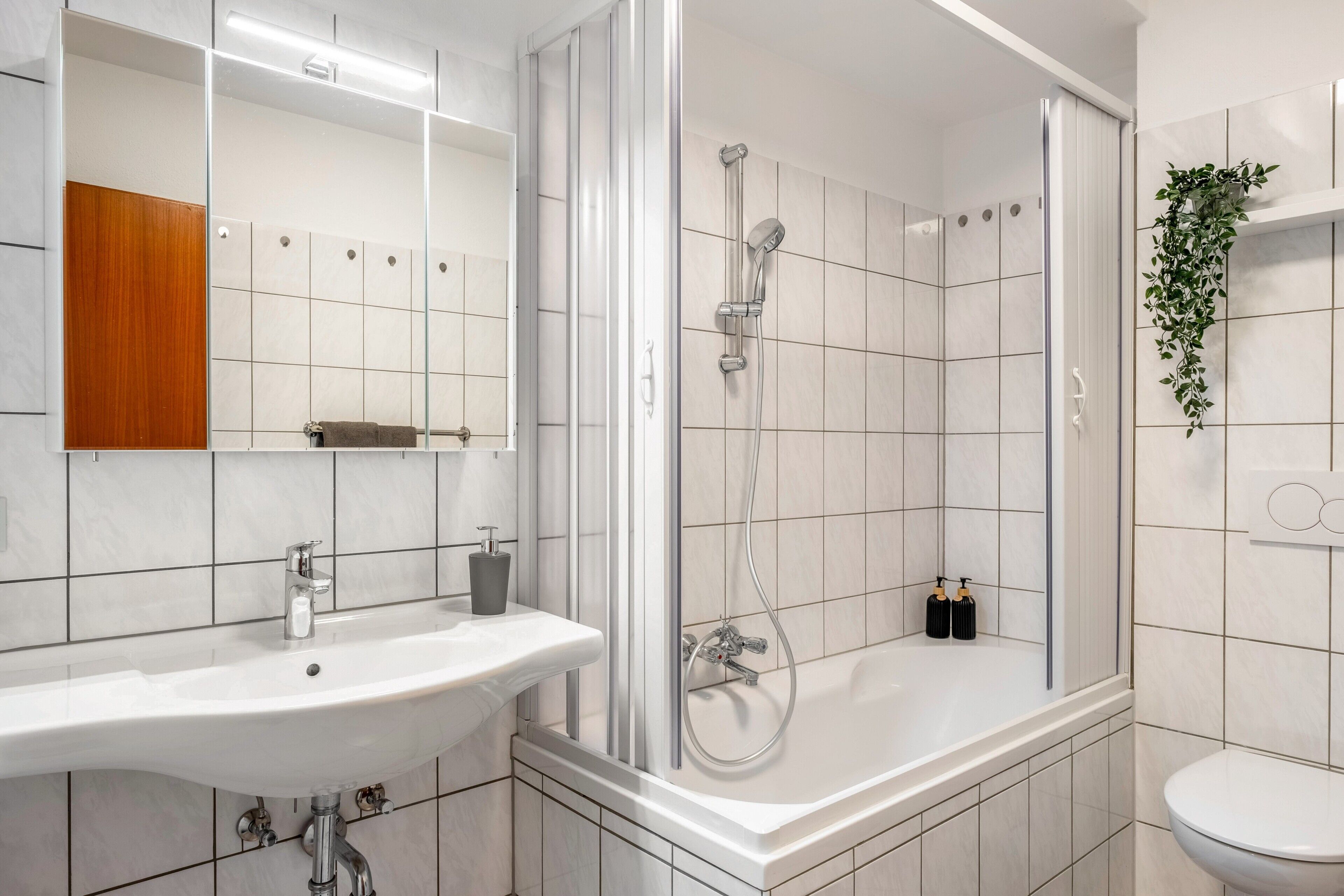 Een moderne badkamer met een douchecabine van glas, een witte wastafel en een toilet.