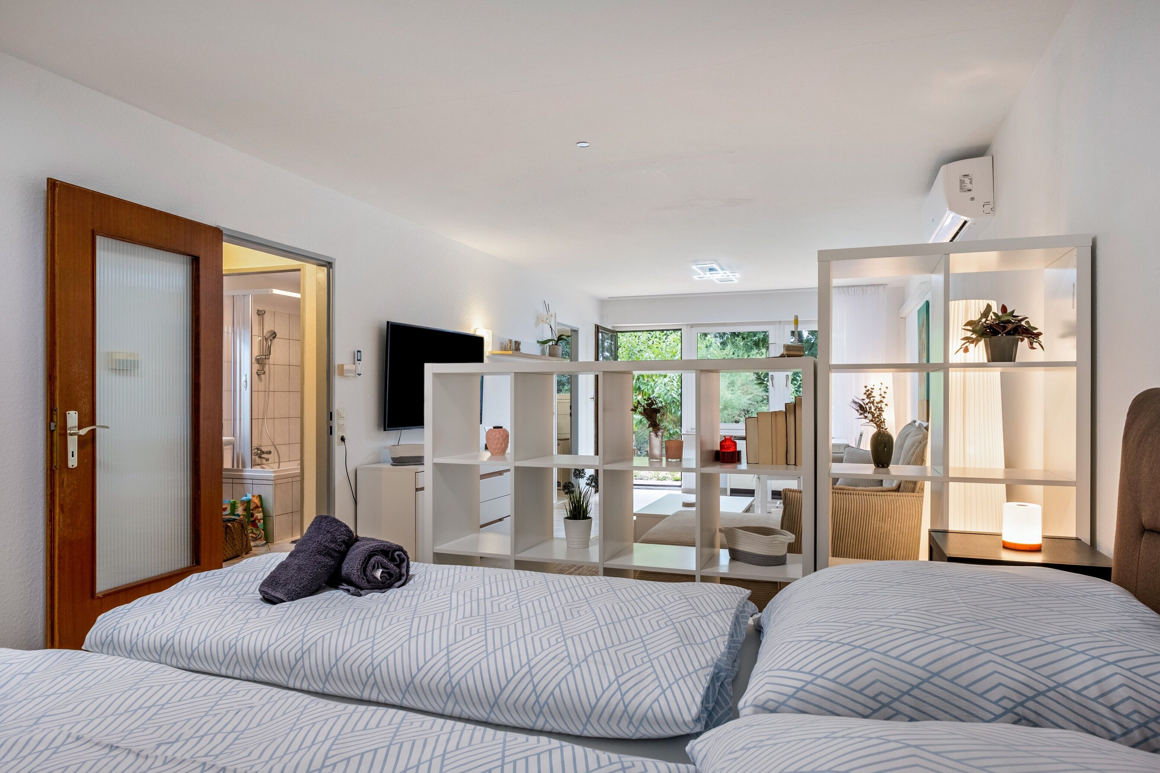 Une chambre à coucher moderne avec un lit, un téléviseur et une bibliothèque intégrée agrémentée de plantes.