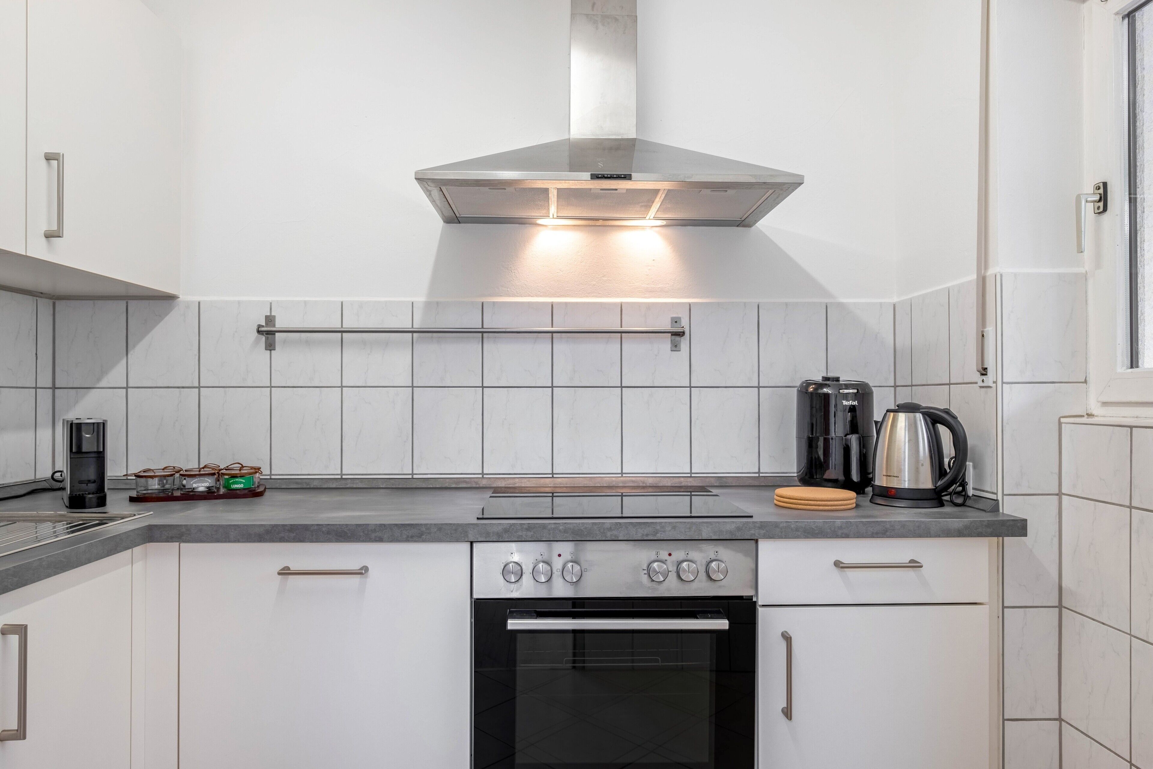 A modern kitchen with a stainless steel range hood, a coffee maker, a kettle, and a toaster.