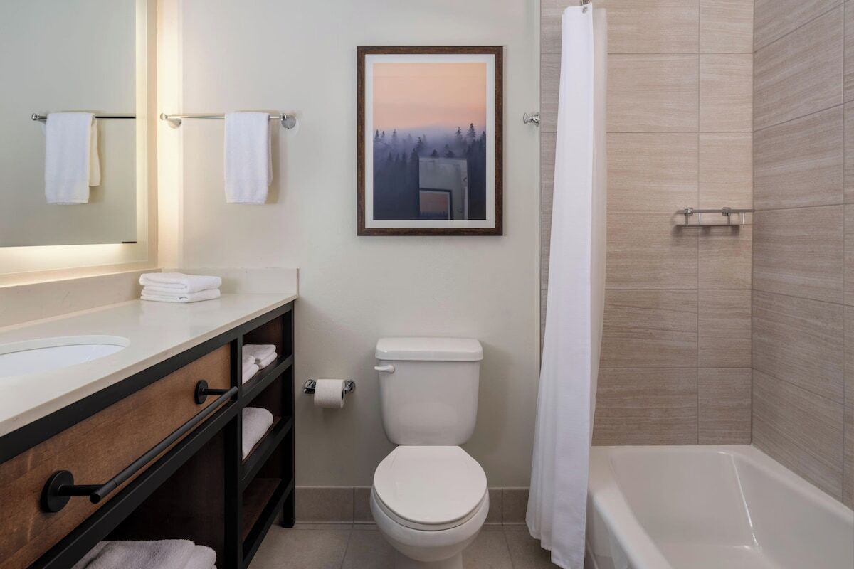 Ein Badezimmer mit Toilette, Waschbecken und Badewanne. Ein gerahmtes Bild hängt an der Wand, und ein Handtuchhalter ist vorhanden.