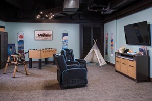 Ein Zimmer mit Massagesessel, Kicker, Fernseher und Bücherregal.