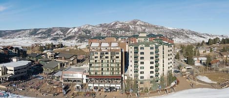Une station de ski avec un grand bâtiment, peut-être un hôtel, entourée de montagnes enneigées et d’une piste de ski.