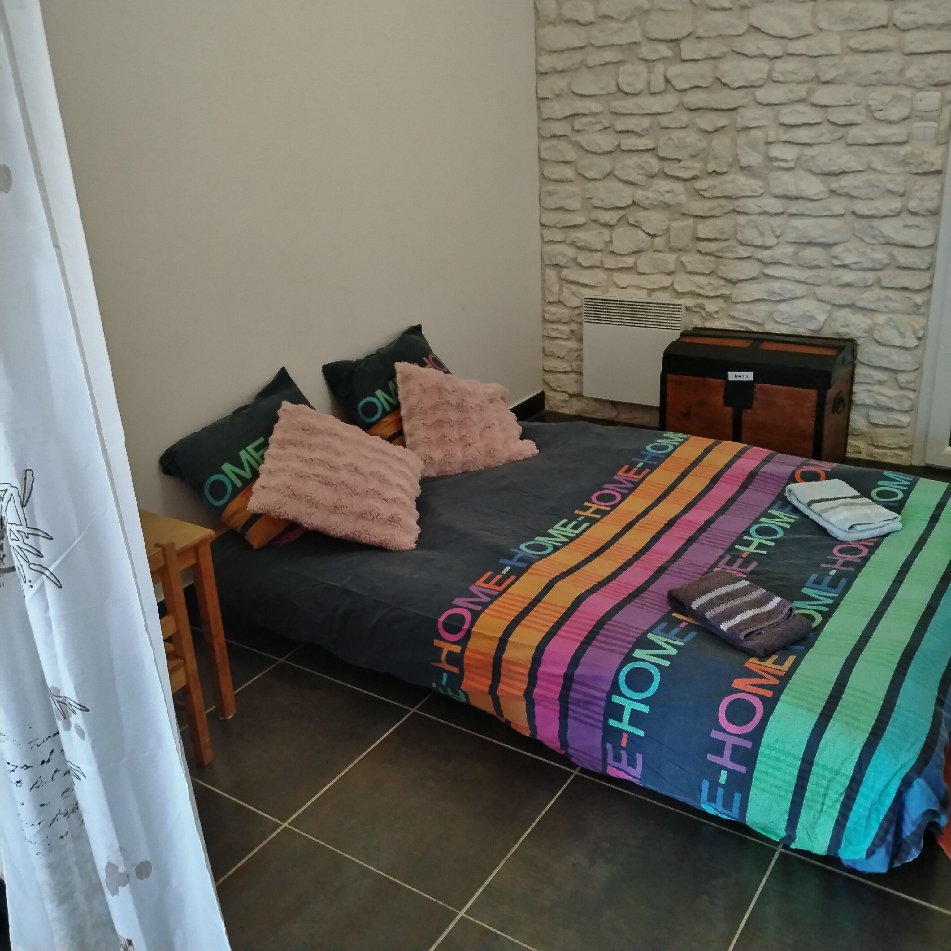 A bed with a colorful striped bedspread, two pillows, a suitcase, and a small wooden stool.