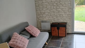A modern living room with a grey sofa, two pink cushions, a wooden cabinet, and a stone wall.