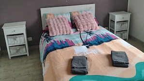 Une chambre à coucher comprenant un lit, deux tables de chevet, une œuvre d’art accrochée au mur et une couvre-lit à motifs.