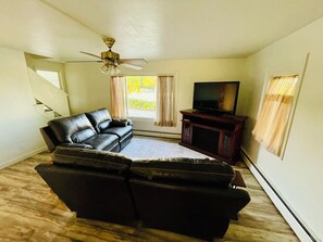A living room with a sofa, a television on a stand, a ceiling fan, and a window with curtains.