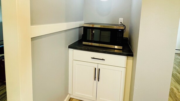 A compact kitchenette with a microwave, a small countertop, and a pendant light.