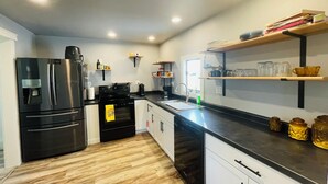 A modern kitchen with a stainless steel refrigerator, a black stove, and wooden flooring.
