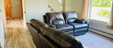 A living room with a sectional sofa, a ceiling fan, and a large window with curtains.