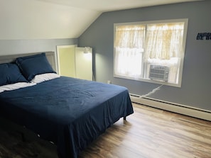 A bedroom with a bed, a window with curtains, a wall-mounted air conditioner, and a sign on the wall. - 3BR Home Near Hahns Lake – Newly Updated Kitchen (Johnson Creek)