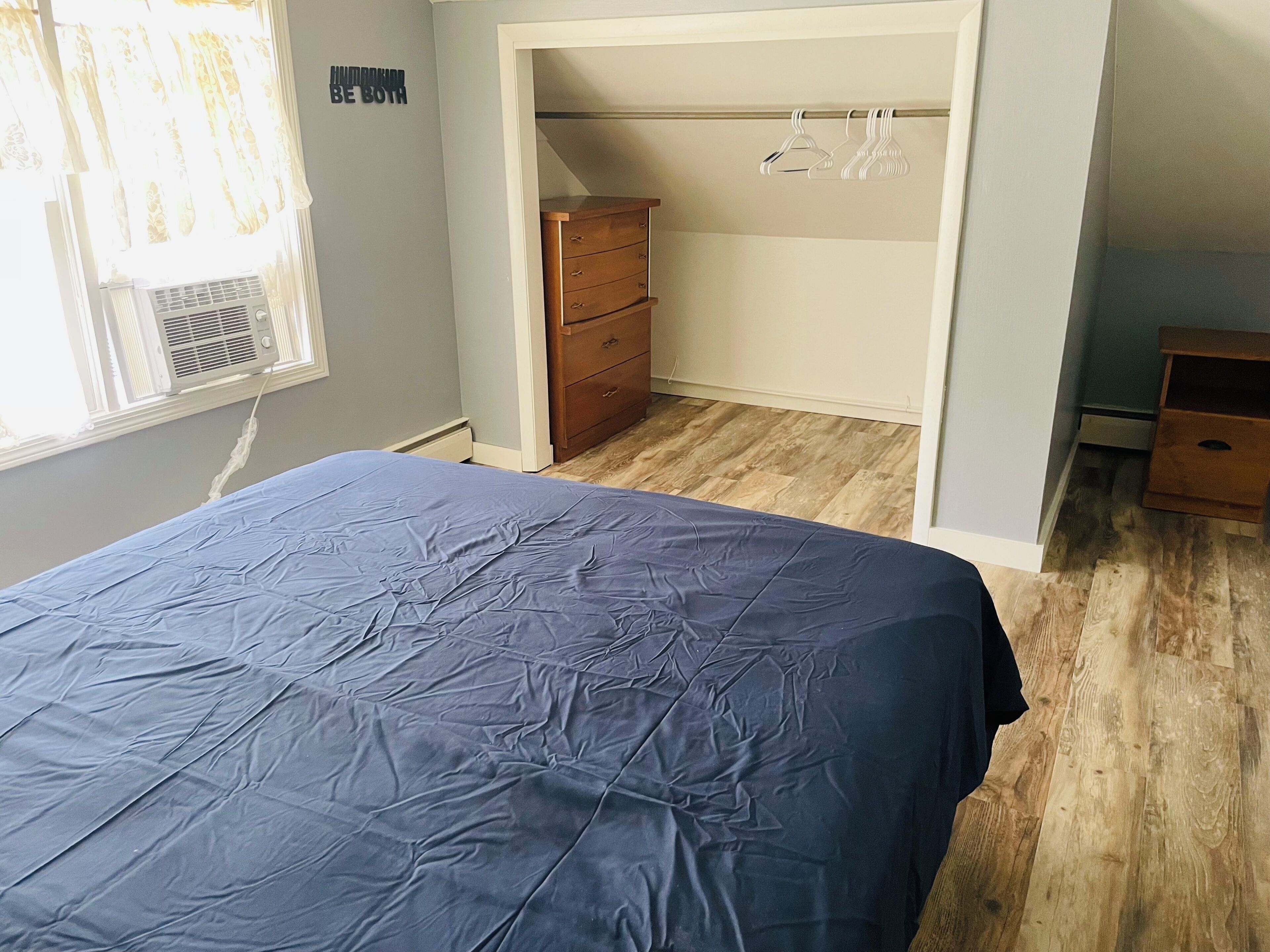 Un dormitorio con cama, cómoda y armario con perchas.