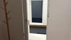 Une pièce avec un plancher en bois, une porte blanche et une fenêtre donnant sur un balcon.