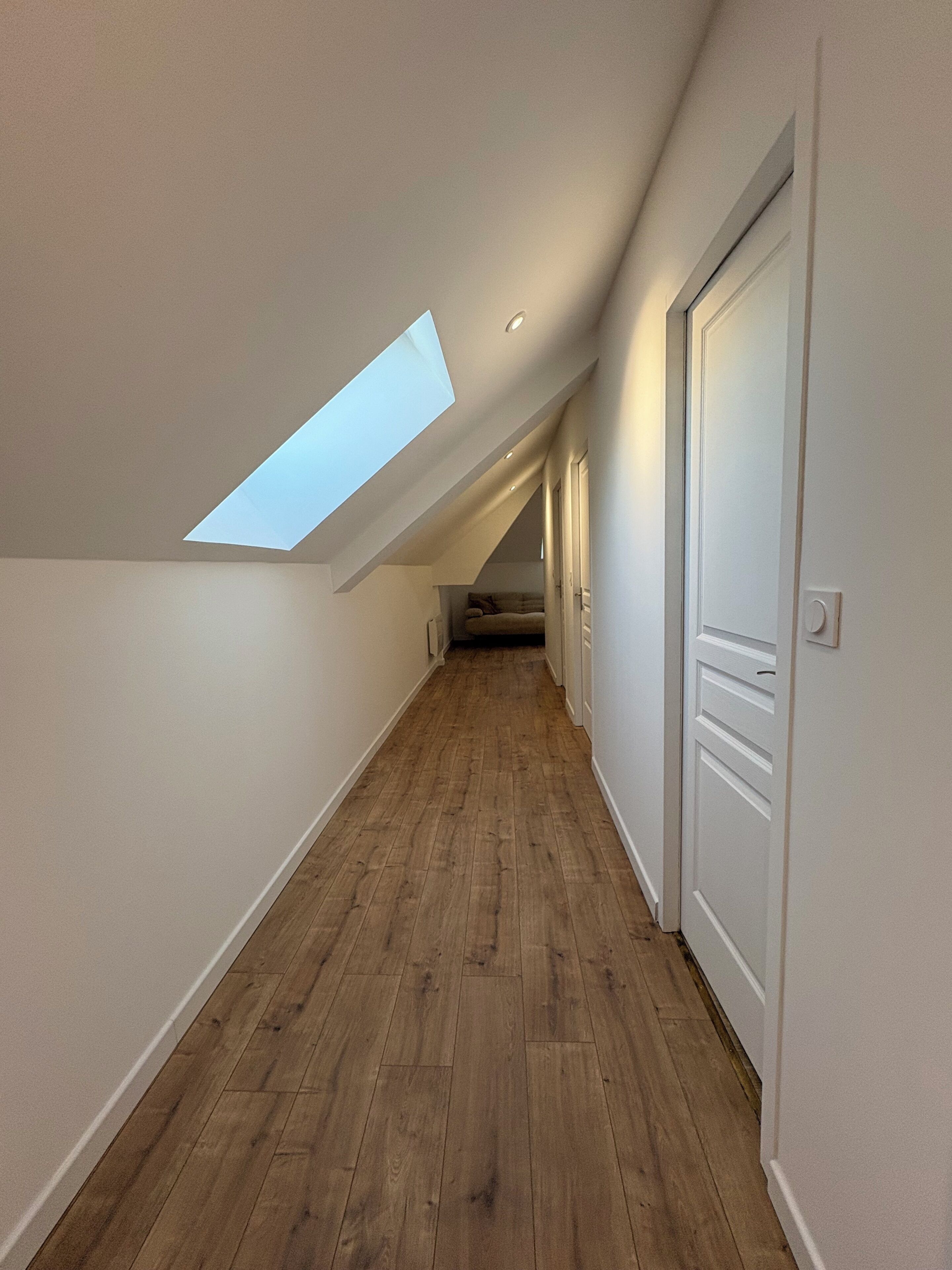 A narrow hallway with wooden flooring, white walls, and a skylight.
