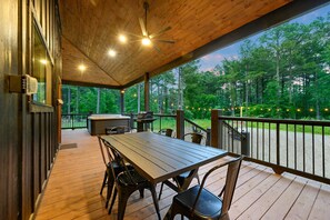 A covered outdoor area with a wooden deck, a table with chairs, a grill, and a hot tub. - NewLuxCabin~PICKLEBALL~Hottub~3Fireplaces~GameRoom~6Beds (Broken Bow)