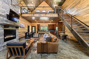 A spacious cabin interior with a fireplace, a dining area, a sofa, and a staircase. - NewLuxCabin~PICKLEBALL~Hottub~3Fireplaces~GameRoom~6Beds (Broken Bow)