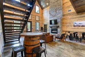Un intérieur spacieux avec une cheminée, des murs en bois, un mur d’accent en pierre et une grande fenêtre.