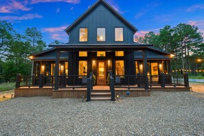 A two-story wooden building with a porch, a welcome sign, and a gravel driveway. - NewLuxCabin~PICKLEBALL~Hottub~3Fireplaces~GameRoom~6Beds (Broken Bow)