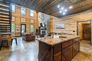 A spacious interior with a large wooden dining area, a fireplace, and a bar area with stools. - NewLuxCabin~PICKLEBALL~Hottub~3Fireplaces~GameRoom~6Beds (Broken Bow)