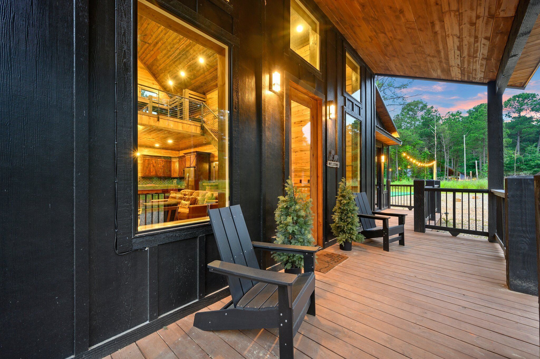 A wooden cabin with a deck, a staircase leading to an upper level, and a welcome sign.