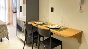 Habitación de hotel con una mesa de comedor preparada para dos personas, una cama, una mesita de noche, un espejo y un teléfono.