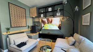 Un saló modern amb un sofà gris, una taula de centre petita, un televisor de pantalla plana muntat a la pared i una estanteria amb objectes decoratius.